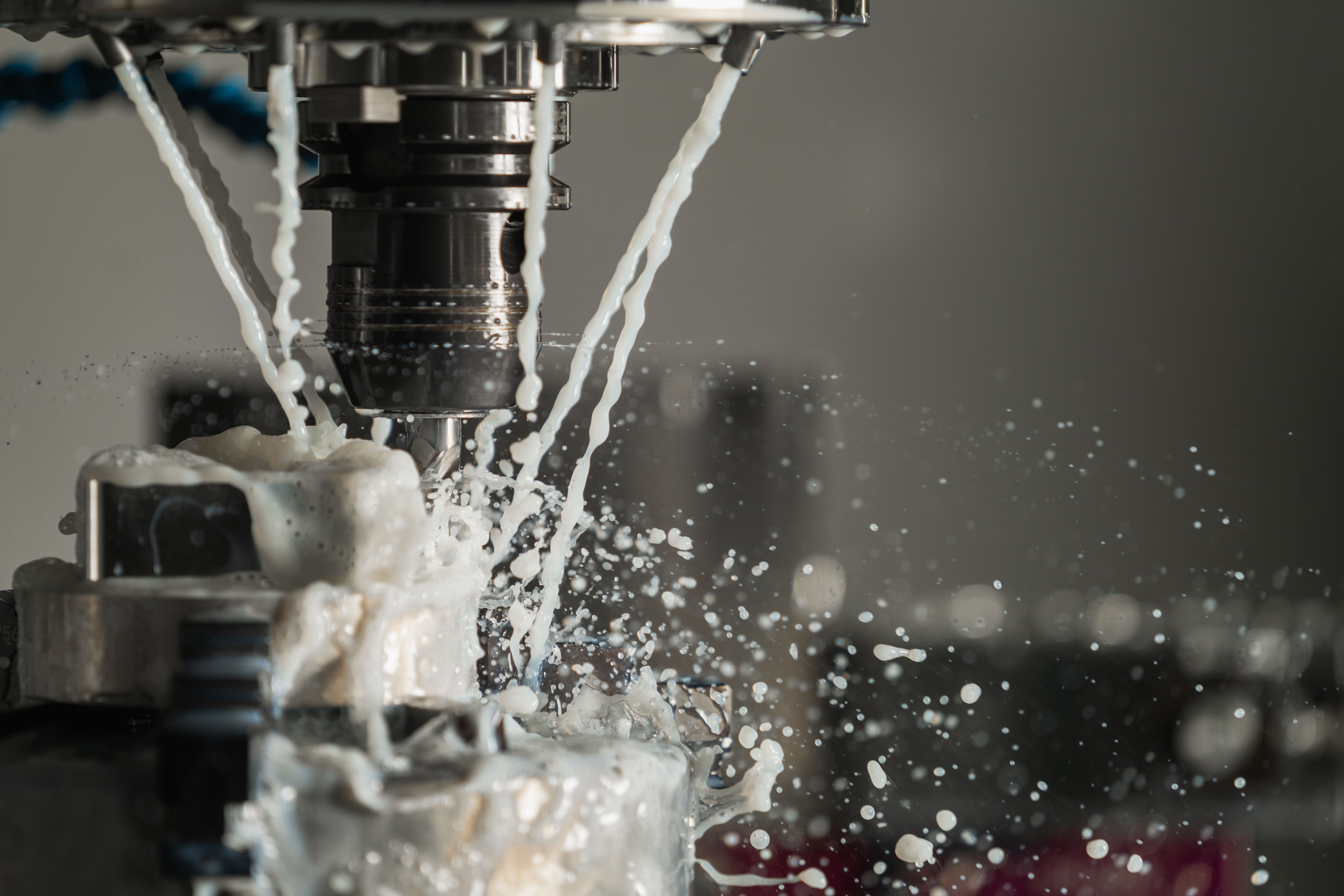 Coolant flooding over a cutter partway through a cut, with spray thrown across the machine bed.