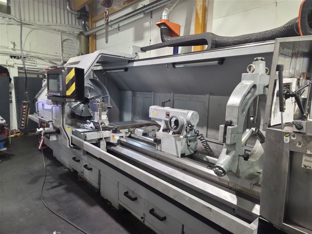 A long-bed lathe with its guard open, showing the chuck, carriage and tailstock.