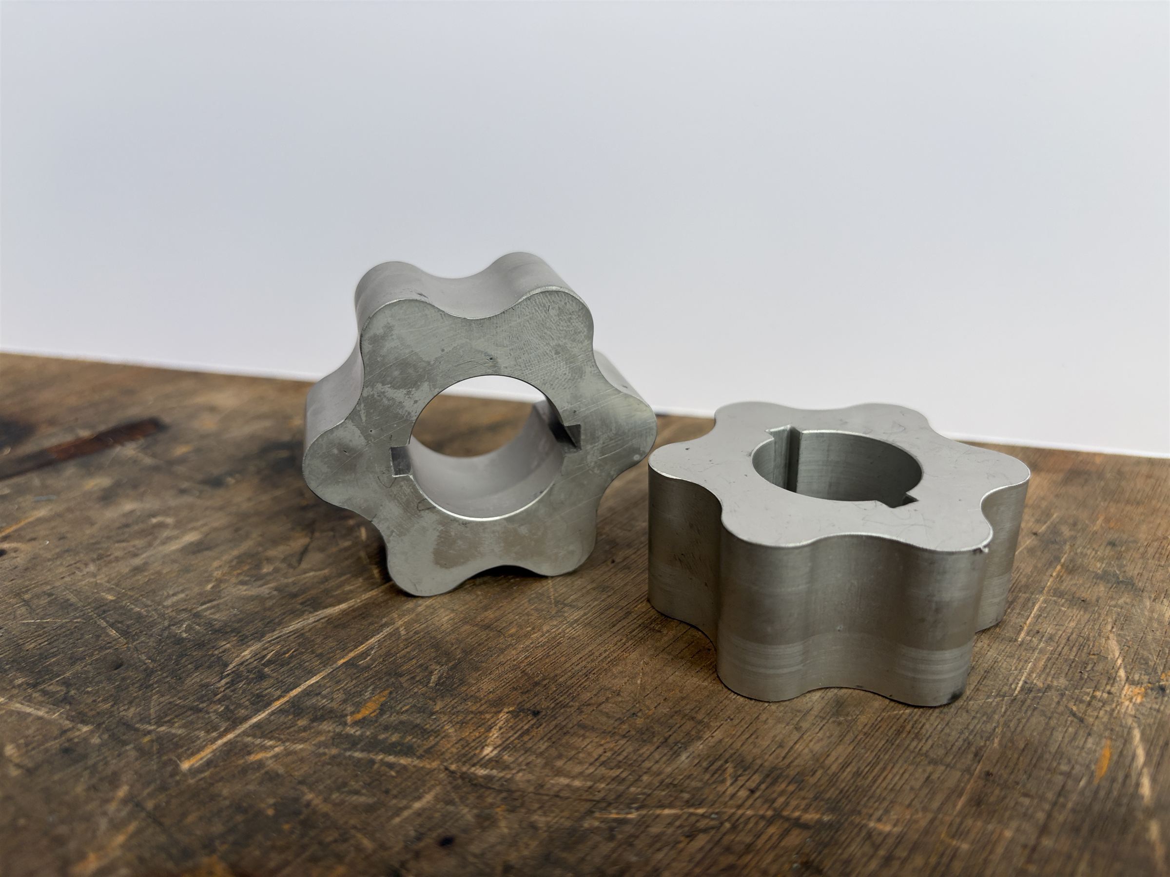 Two machined inner pump rotors on a wooden bench, each with a keyway cut into its bore.