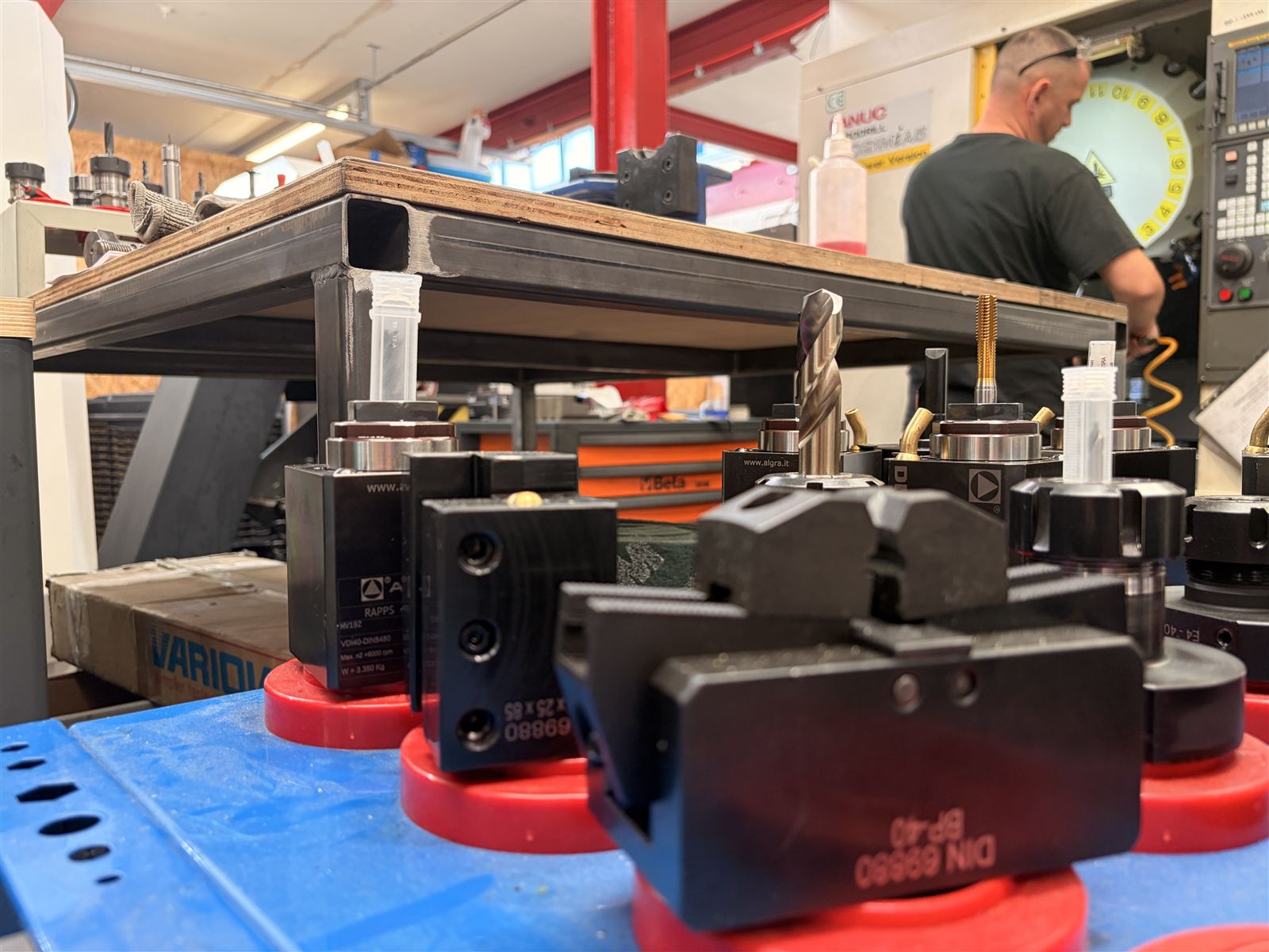 Toolholders lined up on a bench in the foreground while someone works at the FANUC Robodrill behind them.